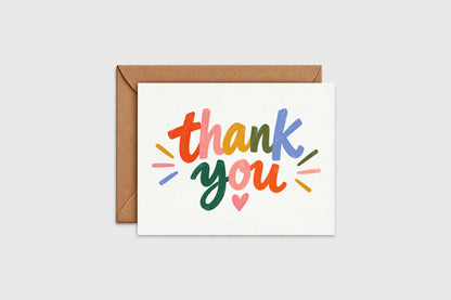 Colorful hand lettered thank you card with rainbow lettering and a small pink heart on white background