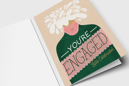 You're Engaged Let's Celebrate card with a popping green champagne bottle on blush