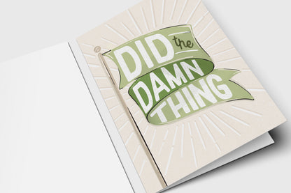 'Did the Damn Thing' congrats card with a green flag banner over an embossed sunburst on cream