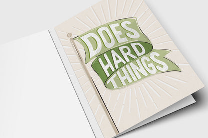 'Does Hard Things' green flag encouragement card with a green banner over an embossed sunburst