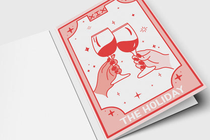 'The Holiday' tarot-style holiday card in pink and red with two hands clinking wine glasses