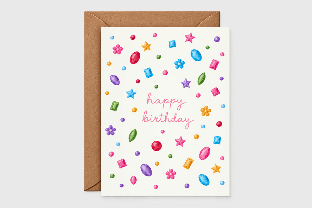 Happy birthday card with colorful watercolor gems, stars and flowers and pink cursive lettering, with kraft envelope