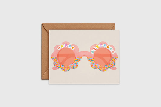 Happy Birthday card with peach flower-shaped sunglasses and rainbow sprinkle frames, with kraft envelope
