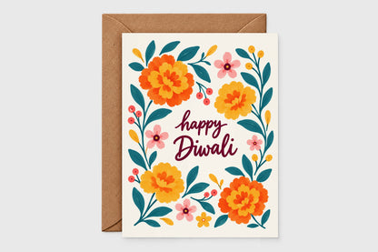 Happy Diwali card with marigold and pink floral wreath design on cream background, kraft envelope behind